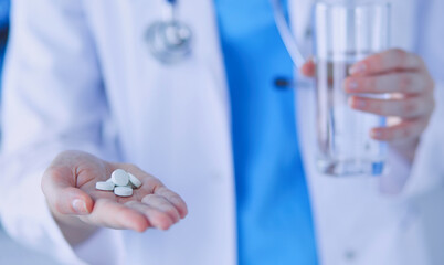 Close-up shot of doctor's hands holding pills and glass of water.