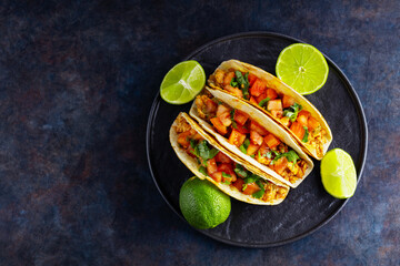 Mexican taco and limes on a dark background. Tacos with minced pork, tomatoes and herbs. Taco with meat and vegetables on a black plate. Copy space. Top view