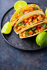 Mexican taco and limes on a dark background. Tacos with minced pork, tomatoes and herbs. Taco with meat and vegetables on a black plate. Copy space. Top view