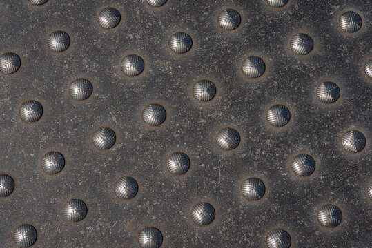 Closeup of a used metal plate with studs as a crossing marker for blind people. Closeup of a metal plate with studs as a crossing marker for blind people. 
The plate is in the sidewalk of a Dutch city