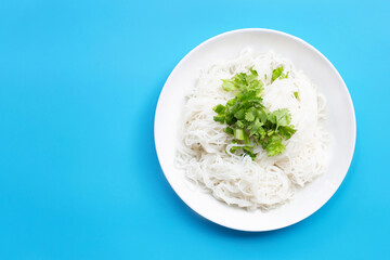 Rice noodles with coriander and spring onion leaves in white plate on blue background.