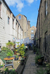 back alley between streets with rows of traditional stone houses in hebden bridge west yorkshire with washing drying on lines and pot plants in bright summer sunshine