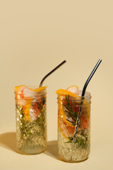 Two drinking glasses of detox water. Infused water with grapefruit slices and rosemary. Healthy summer drinks on minimal beige background. 