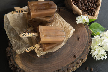 Stack of mocha popsicles on brown parchment paper and a wood slice cutting board accompanied by fresh white hydrangea blooms and bag of coffee beans.