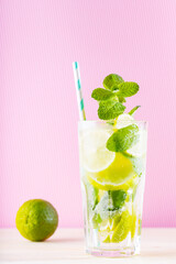 Summer mojito cocktail in a tall glass. Mojito cocktail on a pink background. Refreshing drink with lime, mint and ice. Trendy beverage