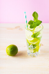 Summer mojito cocktail in a tall glass. Mojito cocktail on a pink background. Refreshing drink with lime, mint and ice. Trendy beverage