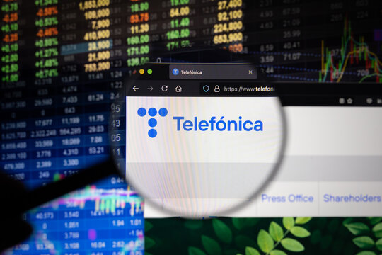 Telefonica company logo on a website with blurry stock market developments in the background, seen on a computer screen through a magnifying glass