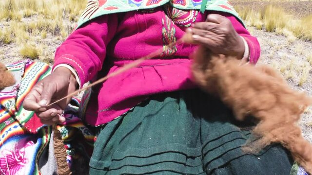 Andean woman spinning alpaca fiber by hand surrounded by an Andean landscape of Peru
