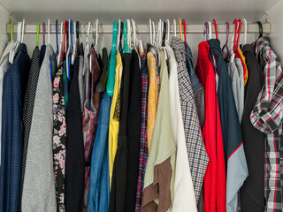 wardrobe closet filled with clothes hanging on hangers, lack of space in the closet, excess clothing, space saving