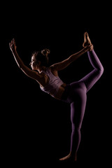 Fit girl practicing yoga in a studio. Half silhouette side lit fitness model...