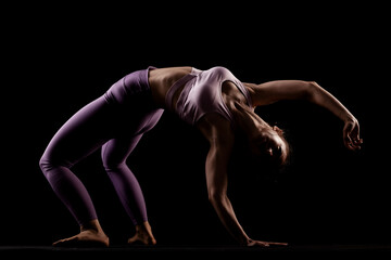 Fototapeta na wymiar Fit girl practicing yoga in a studio. Half silhouette side lit fitness model...