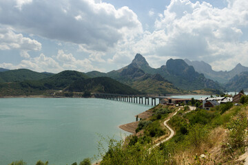 A path runs along the shore of the reservoir to the town. There is a long bridge there that leads to the mountains.