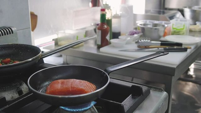 Chef puts red fish fillets in a hot frying pan. Gloves are worn on the hands. Gas stove by the window.