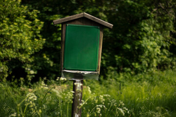 Empty green signboard in meadow with forest on background