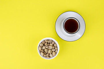 Pistachios in a white plate on a yellow background with a white cup of tea