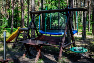 Fototapeta na wymiar Recreational land - space for rest, kids background, slide, trampoline, bench. Place in forest between pine trees.