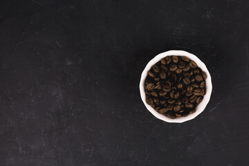 Coffee beans in a white plate on a black background.