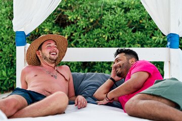 portrait of a homosexual couple of two men lying on a beach bed at a beach club in cancun while...