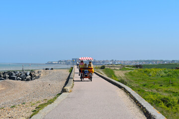 Fototapeta na wymiar Four wheel bike takes holiday makers to the beach huts on the promenade linking Minnis Bay to Reculver abbey The route is used by cyclists walkers bird watchers and is part of the Viking coastal trail