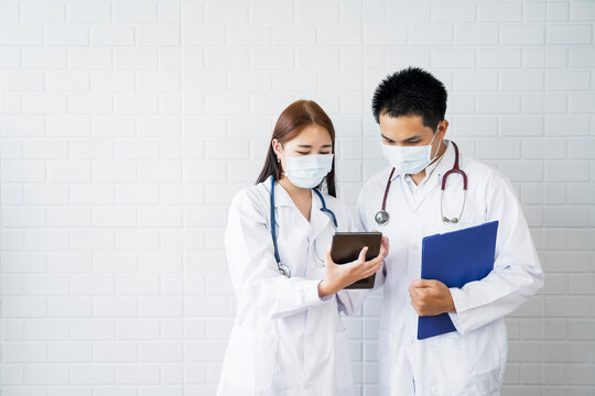 Asian Medical Healthcare Doctor Colleague Teamwork Working Together Examine Diagnosing Discussing Using Tablet Wearing Surgical Mask Work At Home Modern Office Wireless Online Technology Communication