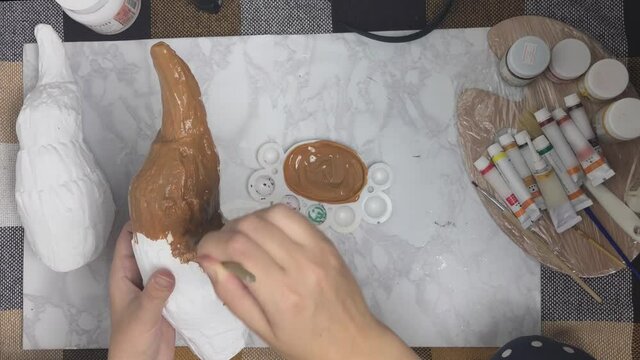 Top view of women's hands paint white antler with brown color. Preparation of props for cosplay. Handicrafts concept. Marble backing and tubes of paint on background.