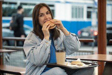 Street portrait of cheerful young woman eating fast food.