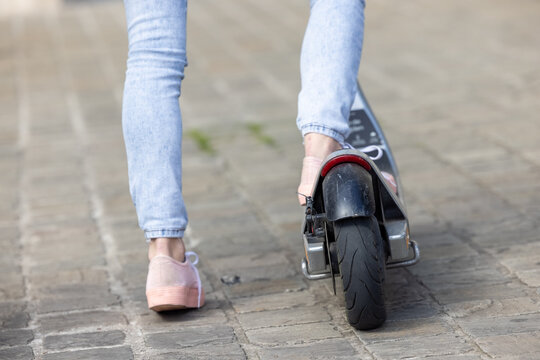 Close-up of female feet of a girl wearing pink sneakers and a jeans on electric kick scooter on the background of the city streets. High quality photo