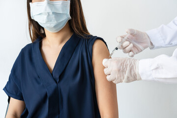 Asian woman in medical mask getting Covid-19 or flu vaccine at the hospital. Hands of male doctor or professional nurse in medical gloves giving antiviral injection to patient.