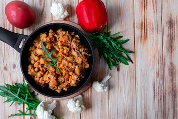 Homemade beef stew with vegetables, potato, onion, carrot, cauliflower, pepper with tomato sauce, garlic and herbs in a cast-iron frying pan on wooden table. Rustic flat lay. Copy space. Top view.