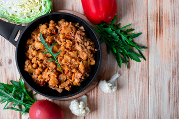 Beef Bourguignon stew with vegetables, potato, onion, carrot, cauliflower, pepper with tomato sauce, garlic and herbs in frying dish on wooden table. Rustic flat lay on wooden background. Copy space.