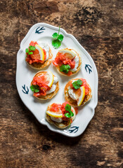Delicious tapas, appetizer, breakfast - mini pancakes with salmon, cream cheese and lemon on a wooden background, top view