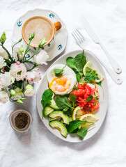 Delicious breakfast, brunch, snack - pancakes with salmon, fresh vegetable salad, poached egg and cappuccino on a light background, top view