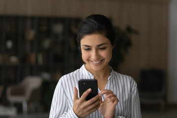 Fototapeta na wymiar Pleasant messaging. Happy young indian woman modern smartphone user chatting texting dating with beloved man online at social network. Smiling teenage female holding virtual dialogue with good friend