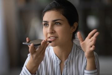 Voice app. Focused millennial indian woman make call using loudspeaker dictating speech message on recorder to send voicemail. Young mixed race lady talk to mobile assistant ai requesting information