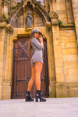 Fototapeta na wymiar Street Style in the city, brunette Caucasian girl with gray dress and a beret, next to a cathedral in a photo pose, lifestyle of a model in the city, vertical photo