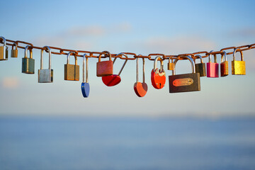 Various and heart colorful shaped love padlocks on a chain on a beautiful blue sky and sea background. Diverse locks as a symbol of togetherness and bonding.