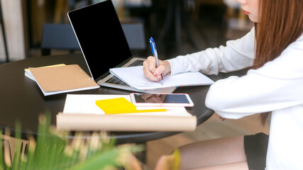 Young adult women hand writing note for study and work online at cafe table with laptop.