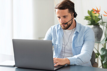 Concentrated freelancer man or support service worker, chatting in a messenger with a client or employees, young male with a beard typing text on laptop sitting at office, online consultation
