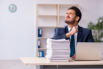 Naklejka premium Young businessman employee and too much work in the office