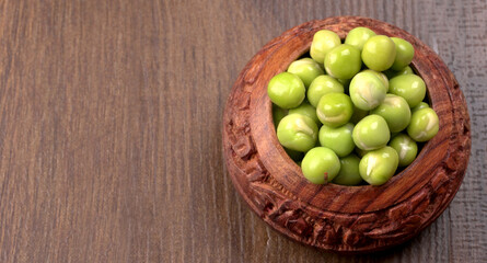 Fresh green peas in wooden bowl on wooden background.