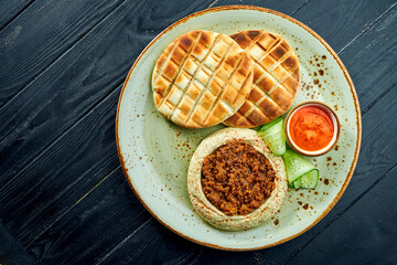 A classic oriental dish - chickpea hummus with olive oil and minced meat served with baked pita in a plate on a dark wood background. Vegetarian food. Diet