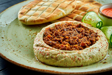 A classic oriental dish - chickpea hummus with olive oil and minced meat served with baked pita in a plate on a dark wood background. Vegetarian food. Diet