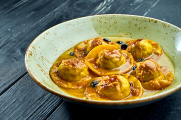 Homemade and mouth-watering ravioli with duck breast and cranberries, served with sauce in a blue plate on a dark wood background. Dish of italian cuisine