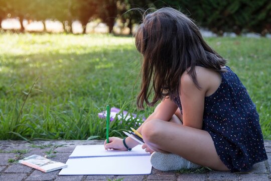 student girl with backpack painting with colored pencils in her notebook, back to school concept