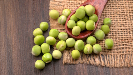 Fresh green peas in spoon on wooden background.