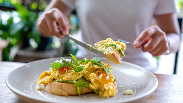 Closeup image of a woman eating scrambled eggs and avocado open sandwich