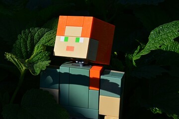 Naklejka premium LEGO Minecraft action figure of Alex, standing in foliage of Lemon Balm and Spearming green herb leaves, dark background. 