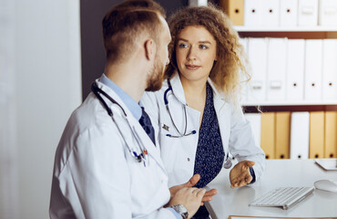 Bearded doctor with female colleague discussing current disease therapy while sitting at working...