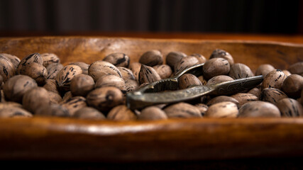 Raw in shell whole Pecan nuts in a wooden bowl on a wood table with a vintage nut cracker