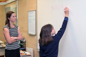 Female student solving a math question on a whiteboard in school calssroom
